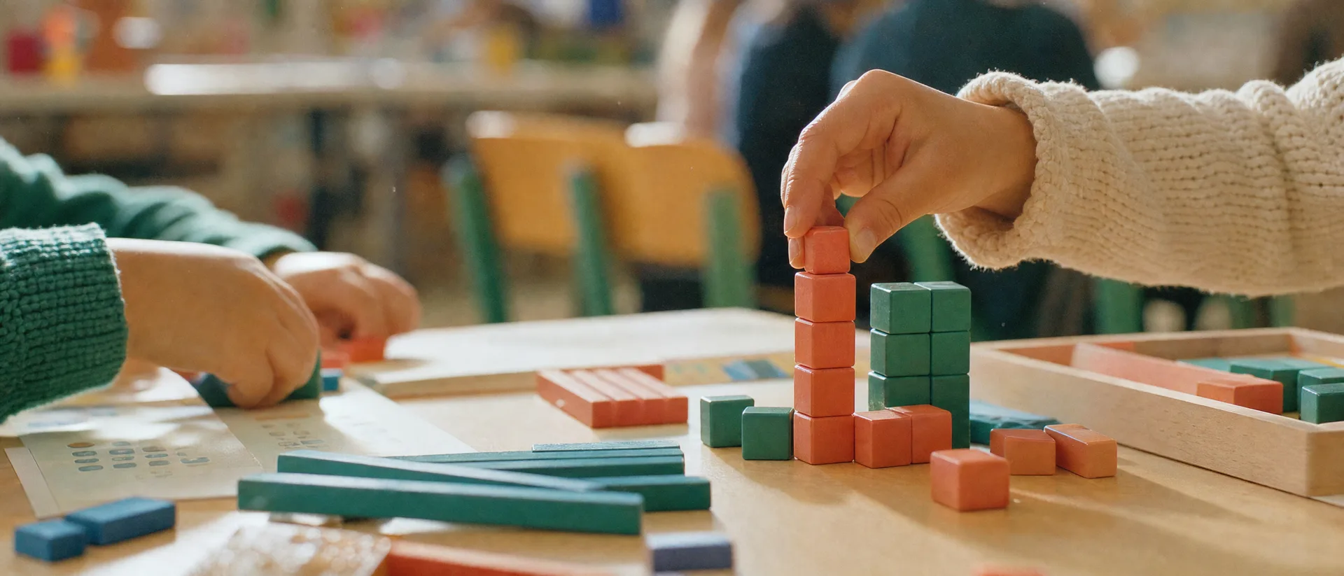 Des mains empilent des cubes de numération sur une table de classe